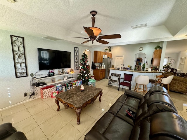 tiled living room with ceiling fan, a textured ceiling, and a tray ceiling