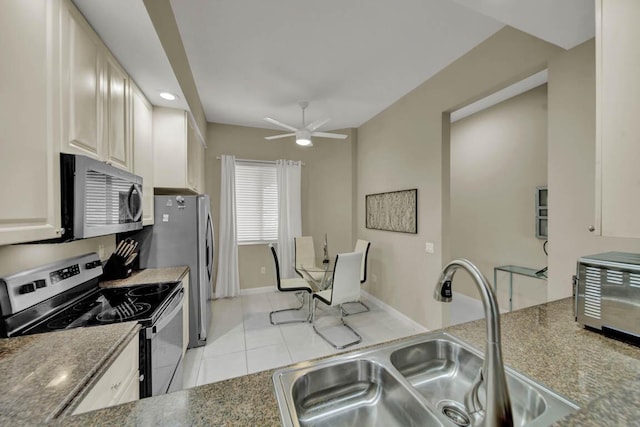 kitchen featuring appliances with stainless steel finishes, ceiling fan, sink, light tile patterned floors, and dark stone countertops