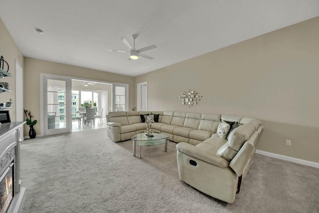 carpeted living room featuring a stone fireplace and ceiling fan