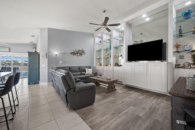 living room featuring built in shelves, ceiling fan, and a textured ceiling