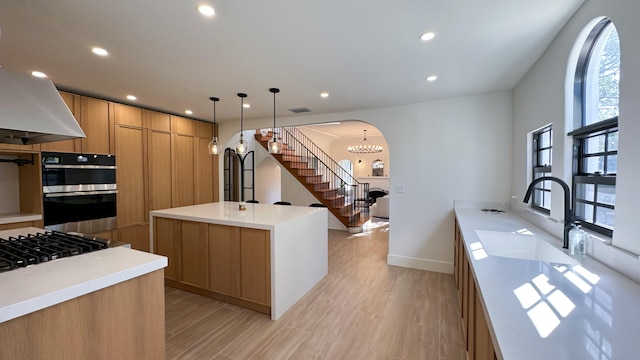 kitchen featuring sink, light wood-type flooring, decorative light fixtures, a kitchen island with sink, and appliances with stainless steel finishes