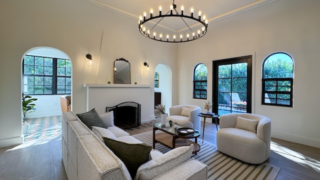 living room featuring wood-type flooring, a high ceiling, a notable chandelier, and ornamental molding