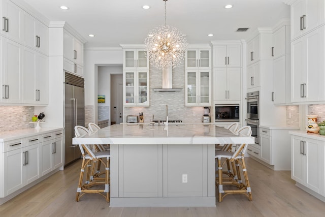 kitchen featuring a kitchen island with sink, decorative backsplash, built in appliances, and pendant lighting