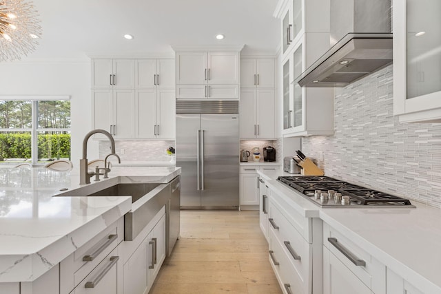 kitchen with appliances with stainless steel finishes, decorative backsplash, wall chimney range hood, white cabinets, and light stone counters