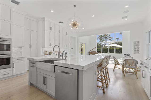 kitchen with appliances with stainless steel finishes, a notable chandelier, a kitchen island with sink, pendant lighting, and sink