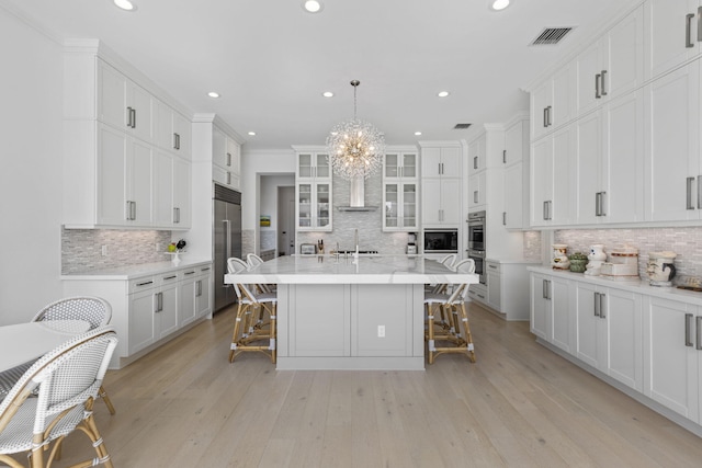 kitchen featuring pendant lighting, built in appliances, white cabinetry, and a center island with sink