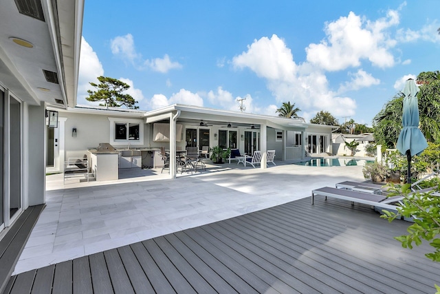 wooden deck with ceiling fan, a patio area, and exterior kitchen