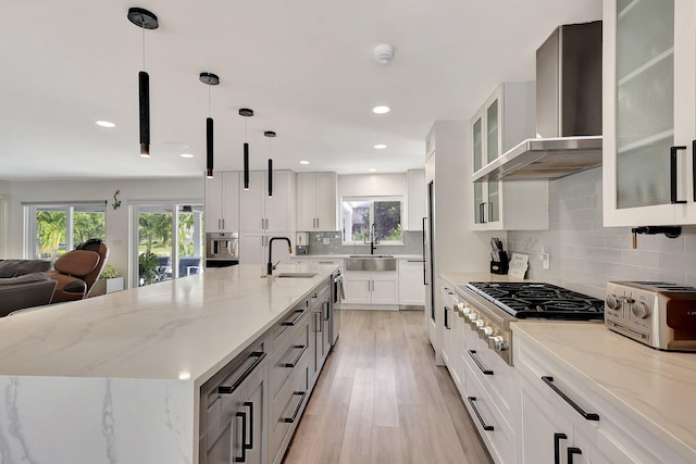 kitchen featuring white cabinetry, hanging light fixtures, a spacious island, and wall chimney range hood