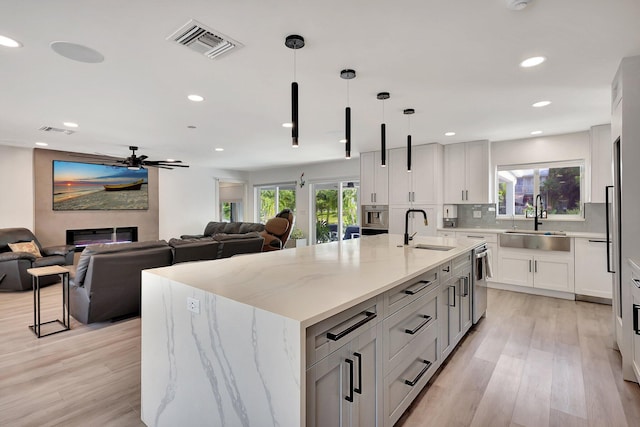 kitchen featuring light stone countertops, sink, light hardwood / wood-style floors, hanging light fixtures, and a large island