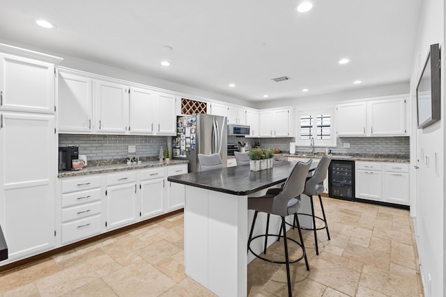 kitchen featuring backsplash, stainless steel appliances, a kitchen island, beverage cooler, and white cabinetry