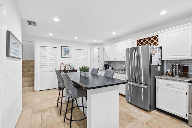 kitchen featuring a center island, backsplash, white cabinets, a kitchen bar, and stainless steel refrigerator