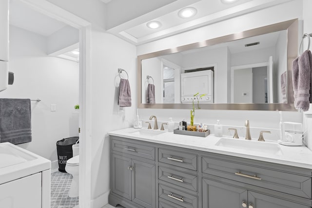 bathroom featuring tile patterned flooring, vanity, stacked washer and dryer, and toilet