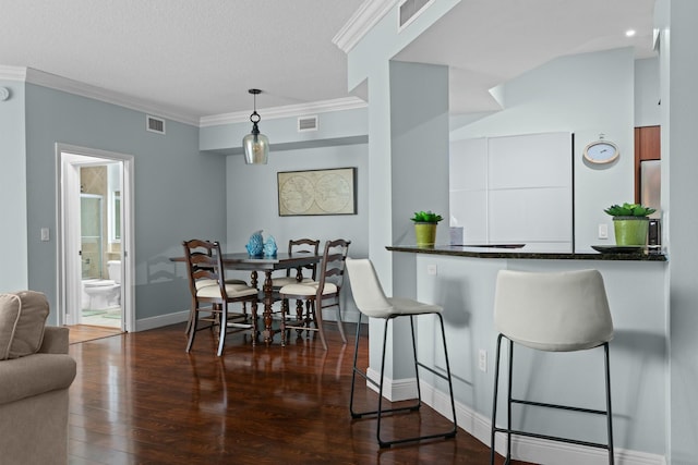 kitchen featuring a textured ceiling, crown molding, dark wood-type flooring, and decorative light fixtures