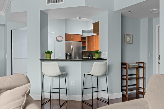 kitchen featuring a kitchen breakfast bar, backsplash, stainless steel fridge, and dark wood-type flooring