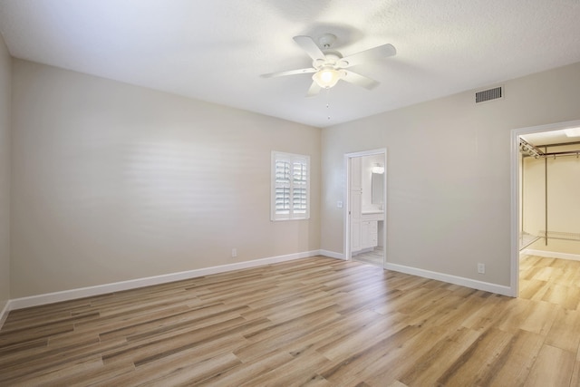 unfurnished bedroom with a walk in closet, light hardwood / wood-style flooring, ceiling fan, connected bathroom, and a closet