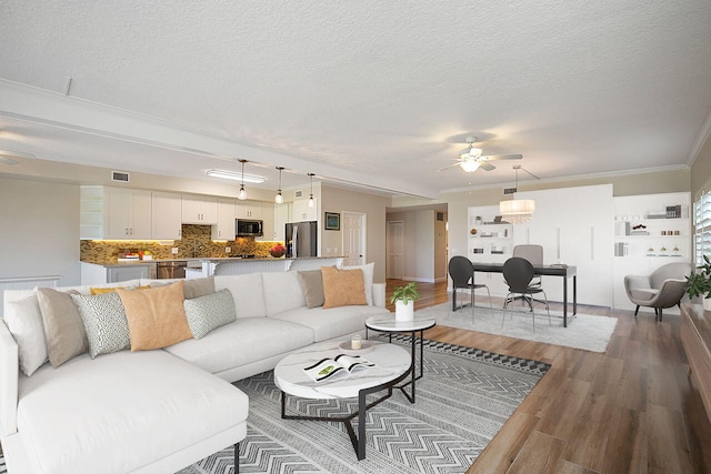 living room featuring hardwood / wood-style floors, ceiling fan, crown molding, and a textured ceiling