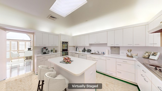 kitchen with a center island, sink, stainless steel double oven, a kitchen breakfast bar, and white cabinets