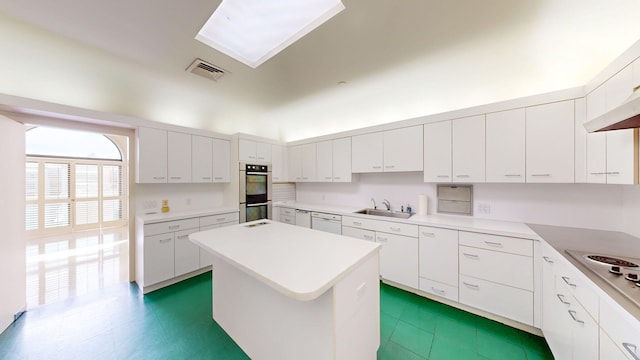 kitchen featuring sink, a center island, a skylight, stainless steel double oven, and white cabinets