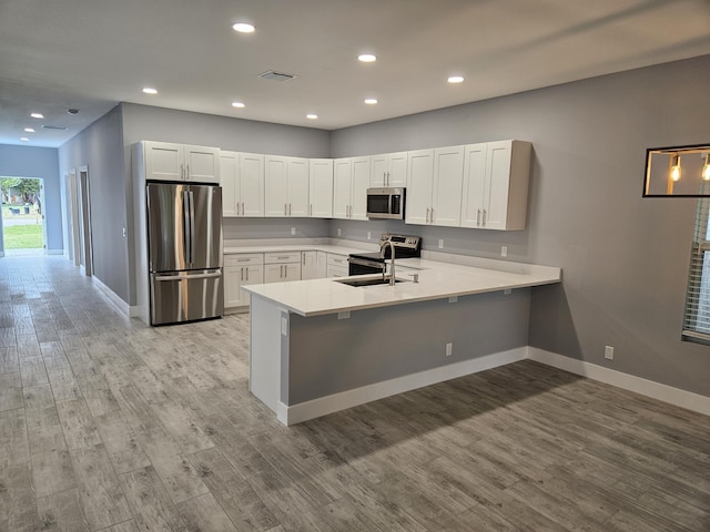 kitchen with sink, stainless steel appliances, kitchen peninsula, light hardwood / wood-style floors, and white cabinets