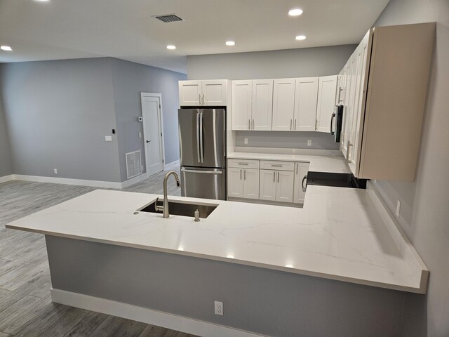 kitchen with sink, light stone counters, light hardwood / wood-style flooring, stainless steel fridge, and white cabinets