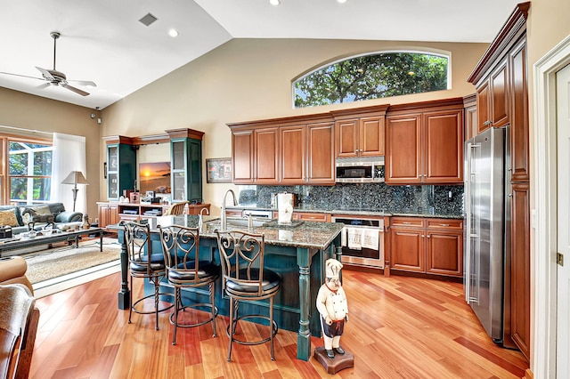 kitchen with a breakfast bar area, light hardwood / wood-style flooring, ceiling fan, tasteful backsplash, and stainless steel appliances