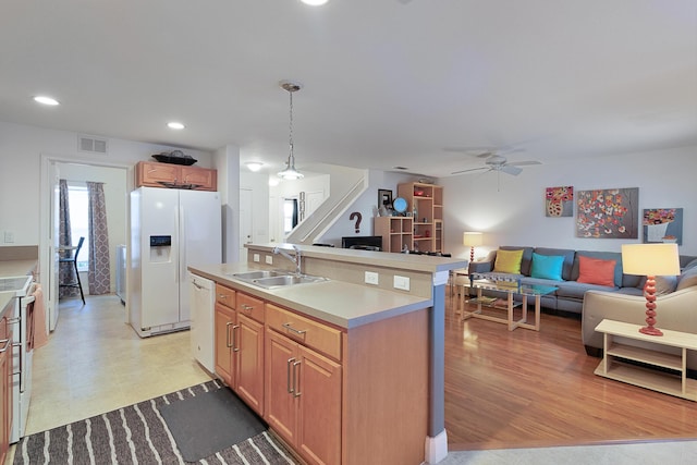 kitchen featuring white appliances, sink, hanging light fixtures, ceiling fan, and an island with sink