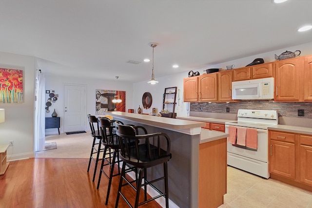 kitchen with decorative backsplash, a kitchen breakfast bar, white appliances, a center island, and hanging light fixtures