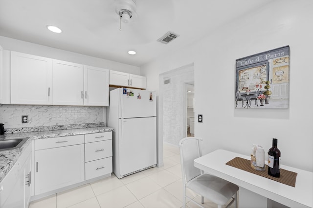 kitchen featuring decorative backsplash, light stone countertops, light tile patterned floors, white cabinets, and white fridge