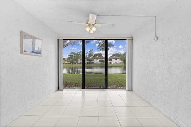 interior space with ceiling fan, a water view, and light tile patterned flooring