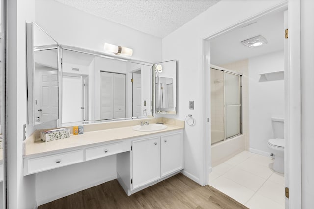 full bathroom with bath / shower combo with glass door, vanity, a textured ceiling, wood-type flooring, and toilet