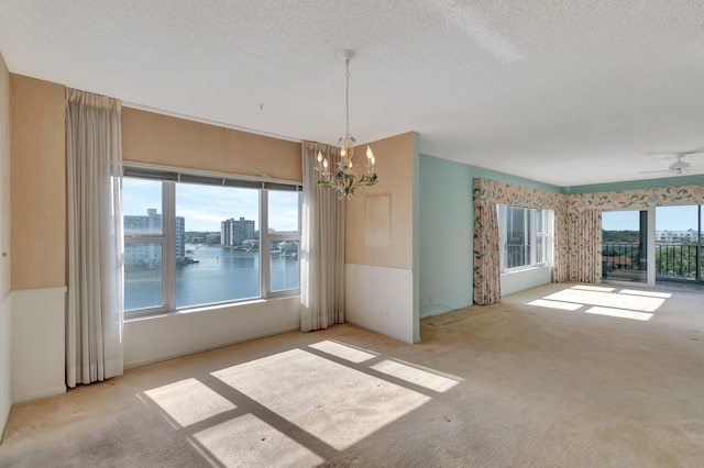 carpeted spare room featuring a water view, plenty of natural light, ceiling fan with notable chandelier, and a textured ceiling