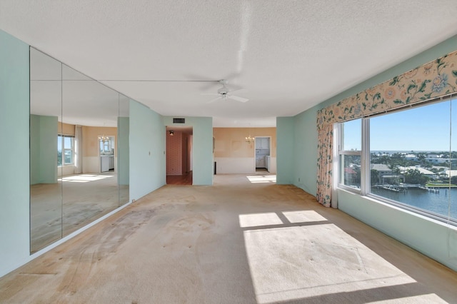 empty room featuring ceiling fan with notable chandelier, light colored carpet, a textured ceiling, and a water view