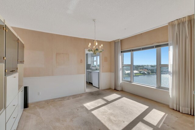 unfurnished dining area with a water view, light carpet, an inviting chandelier, and a textured ceiling