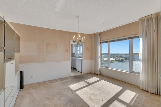 unfurnished dining area featuring a water view, light colored carpet, a textured ceiling, and a notable chandelier