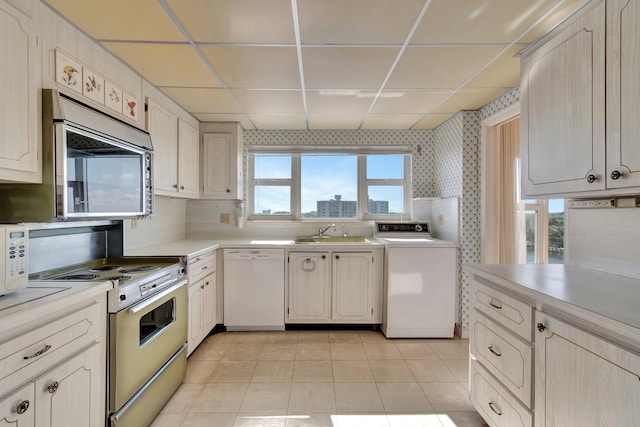 kitchen with light tile patterned flooring, a paneled ceiling, washer / clothes dryer, sink, and white appliances