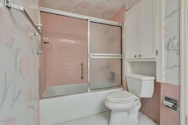 bathroom with tile walls, tile patterned flooring, shower / bath combination with glass door, and toilet