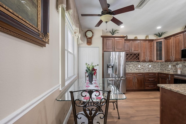 kitchen featuring light hardwood / wood-style flooring, ceiling fan, appliances with stainless steel finishes, tasteful backsplash, and light stone counters