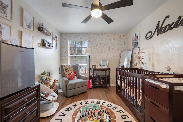 bedroom featuring ceiling fan, light hardwood / wood-style flooring, and a nursery area