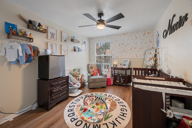 bedroom with hardwood / wood-style floors, ceiling fan, and a nursery area