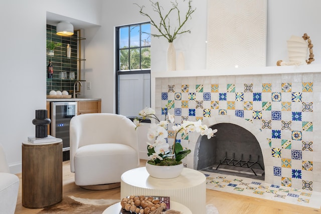 sitting room featuring a tiled fireplace, beverage cooler, and wood-type flooring