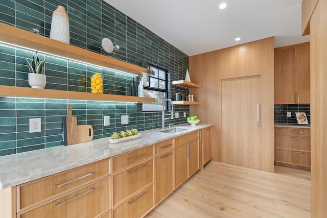 kitchen with light stone counters, sink, backsplash, and light hardwood / wood-style floors