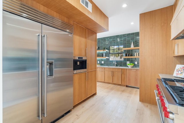 kitchen with light hardwood / wood-style floors, sink, premium appliances, and light brown cabinets