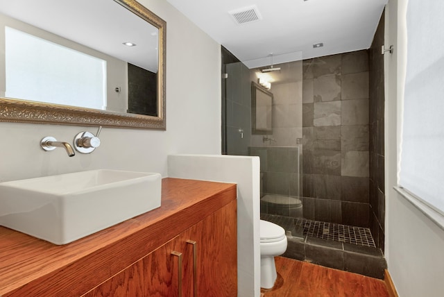 bathroom featuring hardwood / wood-style floors, vanity, toilet, and tiled shower