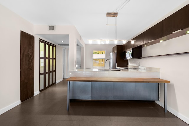 kitchen with kitchen peninsula, dark brown cabinetry, decorative light fixtures, and sink