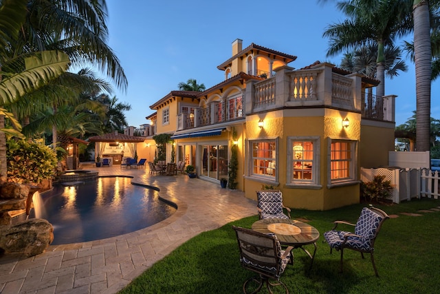 back house at dusk featuring a patio and a balcony