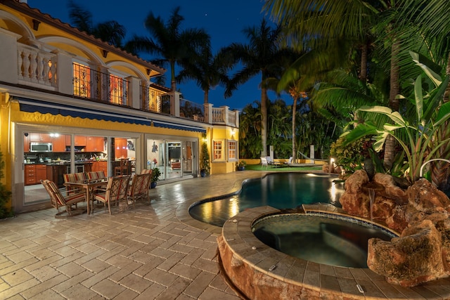 pool at twilight featuring a patio area and an in ground hot tub