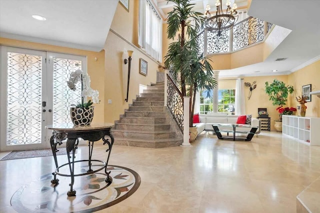 entrance foyer with ornamental molding, french doors, a towering ceiling, and an inviting chandelier