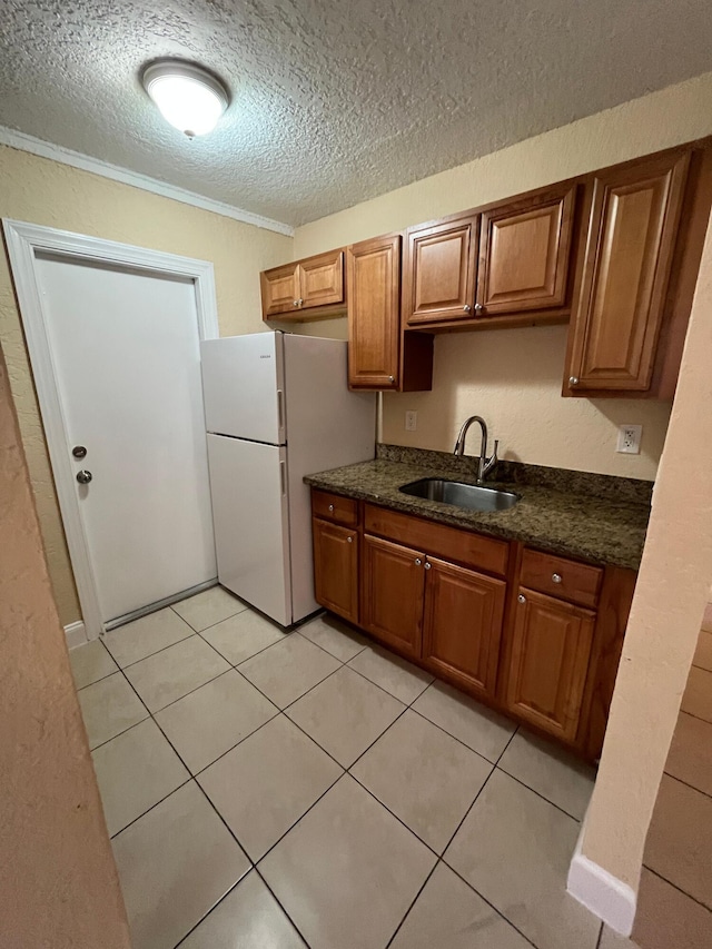 kitchen with white refrigerator, sink, light tile patterned floors, a textured ceiling, and ornamental molding