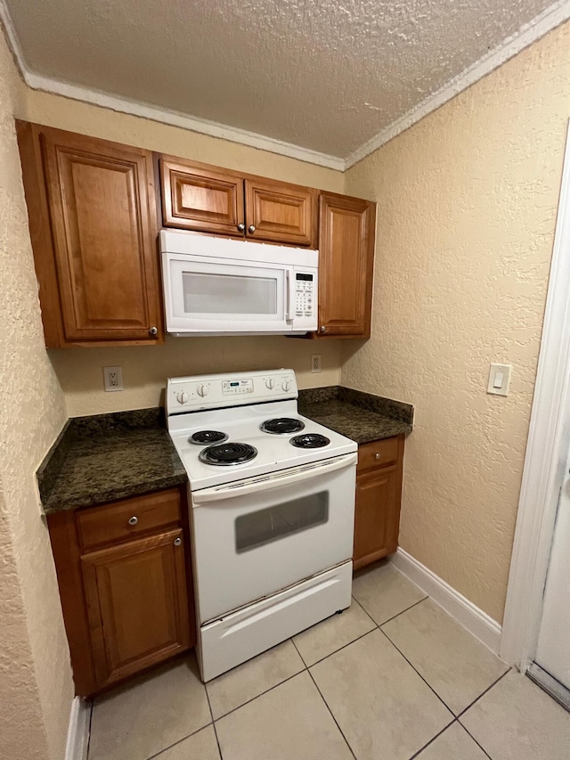 kitchen featuring dark stone countertops, crown molding, a textured ceiling, white appliances, and light tile patterned floors