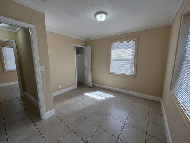 unfurnished bedroom with a textured ceiling, a closet, crown molding, and light tile patterned flooring